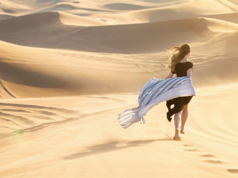 Una chica con un vestido largo negro camina por las dunas